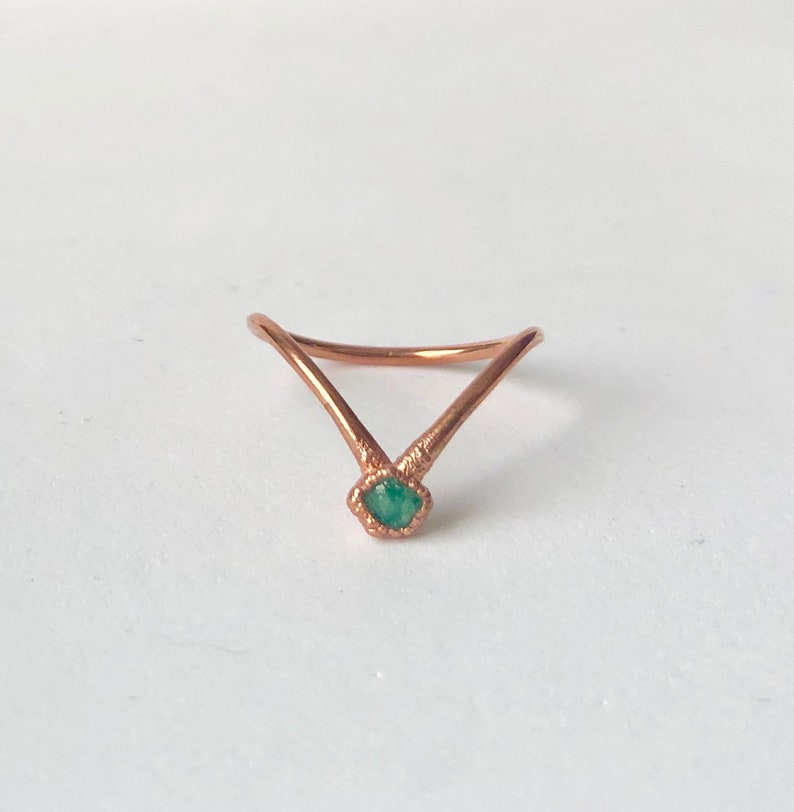 Op de afbeelding: Een koperen ring met een V-vormig ontwerp en een groene edelsteen in het midden.