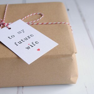 May include: A brown paper gift box tied with red and white twine and a white gift tag that says "to my future wife" with a small red heart.
