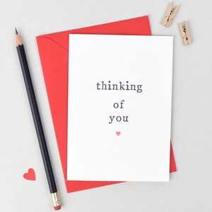 May include: A white card with red envelope. The card has the text "thinking of you" and a small red heart.