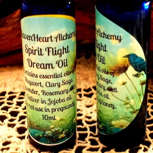 May include: Two dark blue glass bottles of RavenHeart Alchemy Dream Oil. The labels feature botanical illustrations and text, including "Spirit Flight Dream Oil" and essential oil ingredients. Each bottle contains 10ml of oil.
