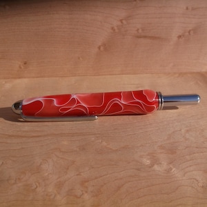 Peut inclure: Un stylo rouge et blanc à motifs tourbillonnants avec une pointe et un capuchon en métal argenté.