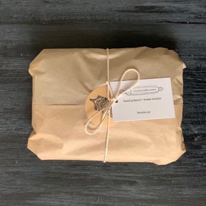 May include: A brown paper package tied with twine and a gift tag. The tag is white with black text that reads "Culture & Butter" and "hand printed + home textiles" and "decatur, ga".