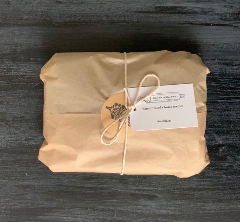 May include: A brown paper package tied with twine and a gift tag. The tag is white with black text that reads "Culture & Butter" and "hand printed + home textiles" and "decatur, ga".