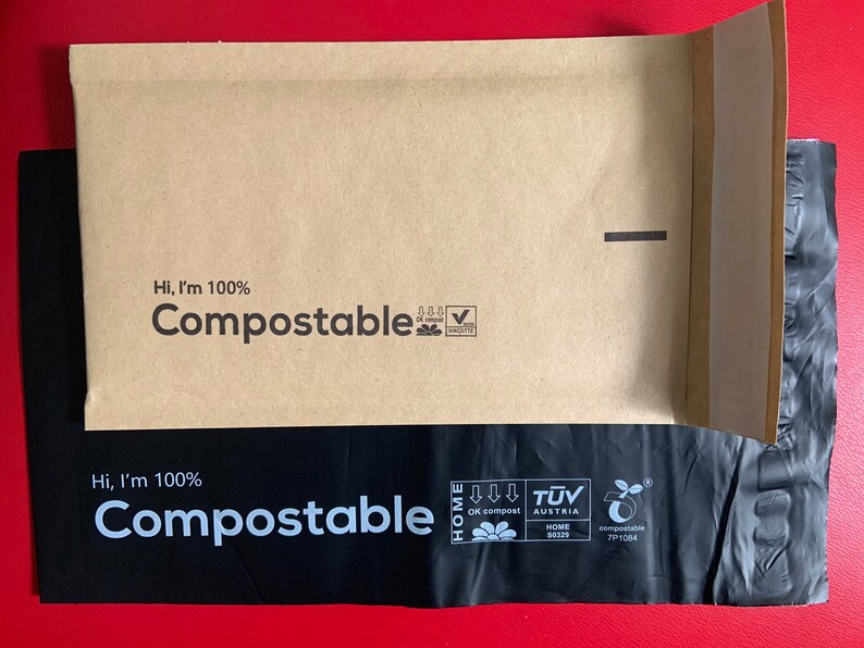 May include: A brown paper envelope with a black plastic liner. Both the envelope and liner have the text "Hi, I'm 100% Compostable" printed on them. The envelope has a seal on the top right corner. The liner has a green leaf logo with the text "OK compost HOME" and "TUV AUSTRIA HOME" printed on it.