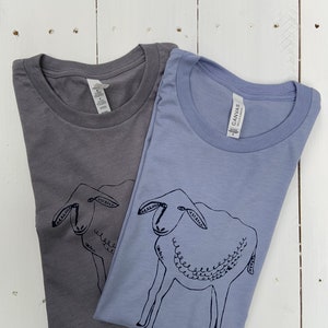May include: Two t-shirts with a simple black line drawing of a sheep on them. The shirts are a light gray and a light blue.