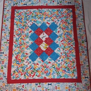 Puede incluir: Una colcha roja, blanca y azul con temática de Dr. Seuss. La colcha está hecha de cuadrados con una variedad de patrones, incluyendo letras, lunares y un personaje de Dr. Seuss. La colcha está bordeada con una tela roja con letras blancas.