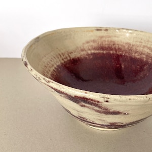 Peut inclure: Un grand bol en céramique blanche avec un glaçage bordeaux foncé. Le glaçage a un effet marbré, avec des stries blanches et bordeaux.