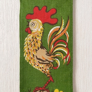 May include: A green fabric with a yellow, red and white rooster design. The rooster is facing left and has a red comb and wattle.
