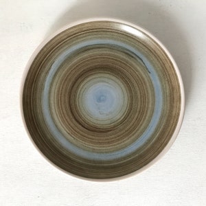 May include: A round ceramic plate with a swirling pattern of brown and blue glaze. The plate has a white rim and a slightly raised center.