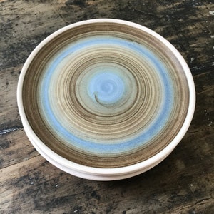May include: A ceramic plate with a brown and blue swirl pattern. The plate has a white rim and is slightly raised in the center.