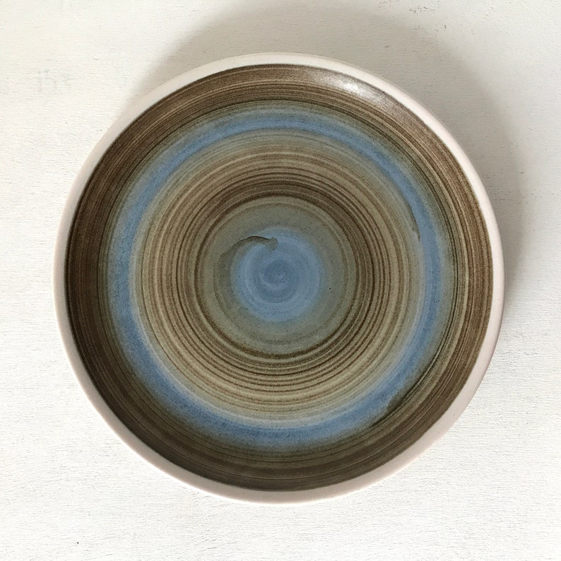 May include: A ceramic plate with a swirling pattern of brown and blue glaze. The plate has a white rim.