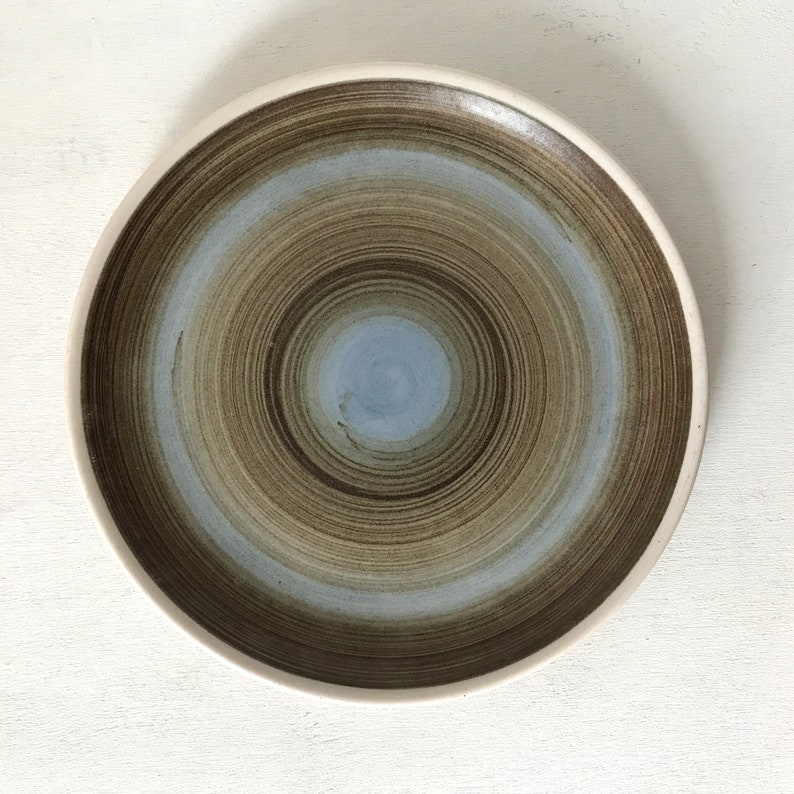 May include: A brown and blue ceramic plate with a swirling pattern. The plate has a white rim and a light blue center.