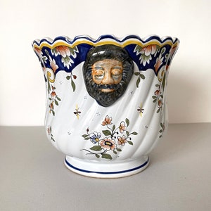 May include: A white ceramic planter with a blue and yellow floral design. The planter has a face with a beard sculpted on the front.