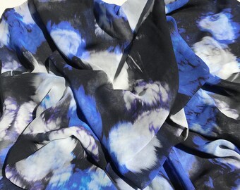 Op de afbeelding: Een blauwe en zwarte stof met een abstract print en een zachte, vloeiende textuur. De stof is doorschijnend en lichtgewicht, waardoor het ideaal is voor sjaals, tops of jurken.