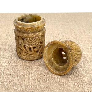 Puede incluir: Un peque&ntilde;o recipiente de piedra beige tallado con tapa. El recipiente tiene intrincados dise&ntilde;os florales y est&aacute; abierto para revelar el interior.