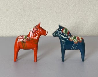 May include: Two traditional Swedish Dala horse figurines, one painted red with white floral details and the other painted blue with white floral details.