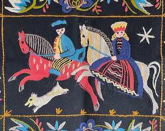 May include: Embroidered wall hanging featuring two figures on horseback, one in blue and one in red, against a black background with floral designs.