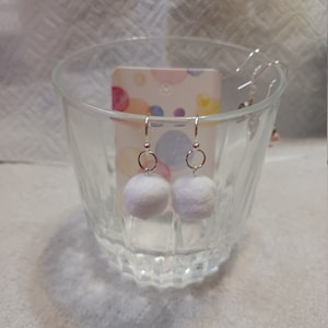 May include: A pair of white pom-pom earrings with silver hoops.