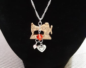 May include: A silver chain necklace with a wooden sewing machine pendant. The pendant has a red crystal and a silver heart charm with a pink pearl.
