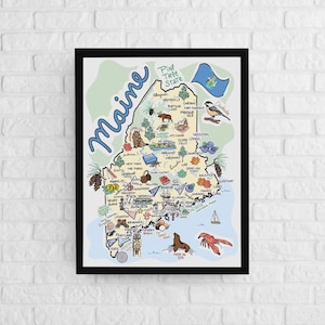 May include: A framed illustrated map of Maine featuring the text Maine and Pine Tree State. The map includes drawings of local landmarks, wildlife like a moose and seal, blueberries, a lobster, and the state flag against a light green background.