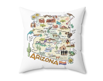 May include: A white square throw pillow featuring a colorful illustrated map of Arizona. The design includes various state landmarks, wildlife, and flora, with the word ARIZONA printed in large orange letters at the bottom and the state flag.