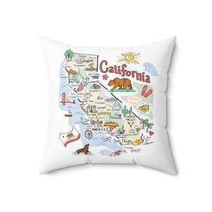 May include: A white square throw pillow featuring a colorful illustrated map of California. The design includes landmarks like the Golden Gate Bridge, a brown bear, a sun, and text labels for cities and regions such as Los Angeles and San Diego.