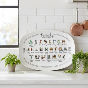 May include: White oval serving platter featuring the "Kentucky Alphabet" with illustrations for each letter. The platter includes images of the state's landmarks and symbols, such as the Kentucky Derby and Mammoth Cave.