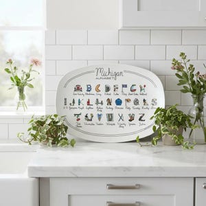 May include: White oval serving platter with a black border and the words "Michigan Alphabet" in a script font. The platter features colorful illustrations representing the alphabet, with each letter paired with a Michigan-related image.