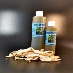 Puede incluir: Dos botellas de Aceite Herbal de Sello de Salomón, una más grande y otra más pequeña, ambas con una etiqueta verde y una tapa blanca. Las botellas están sobre una superficie negra con un montón de raíces secas, de color marrón claro, cortadas delante de ellas.