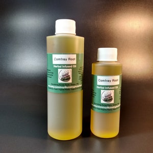 May include: Two bottles of Comfrey Root Herbal Infused Oil. The bottles are clear glass with yellow liquid inside. The larger bottle is 4 oz and the smaller bottle is 2 oz. Both bottles have a white cap and a green label with the company name and website.