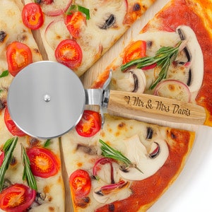 May include: A pizza cutter with a wooden handle engraved with "I Mr. & Mrs. Davis". The cutter is on top of a pizza with red sauce, mushrooms, and cheese.