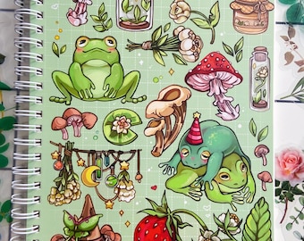 Puede incluir: Una libreta verde con espiral presenta una variedad de ilustraciones caprichosas, incluyendo ranas, hongos, fresas, una polilla y un sombrero de bruja. Las ilustraciones son de estilo de dibujos animados y están rodeadas de un fondo verde con lunares blancos.