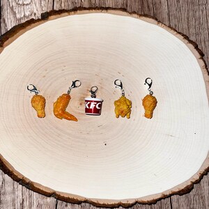 May include: Five charm pendants featuring fried chicken pieces and a red bucket with the KFC logo. The charms are made of resin and have a realistic appearance.
