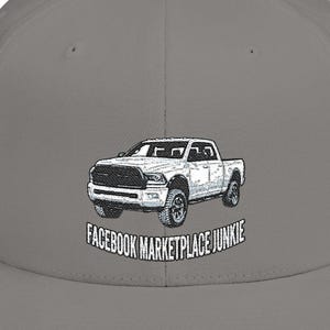 May include: A gray, flat-billed baseball cap featuring a white pickup truck graphic. The text "FACEBOOK MARKETPLACE JUNKIE" is arched below the truck. The cap has a structured fit and a curved brim.