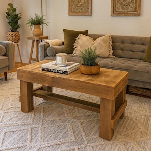 May include: A living room scene featuring a wooden coffee table with a book titled "LIVING WILD" and a small potted plant. A gray sofa with decorative pillows sits behind the table. Two decorative mirrors hang on the wall. A patterned rug covers the floor.