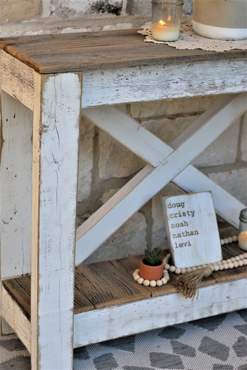 May include: Whitewashed wooden console table with a distressed finish. The table has a shelf and a top made of reclaimed wood. A small potted succulent and a wooden sign with the names Doug, Cristy, Noah, Nathan, and Levi are on the shelf.