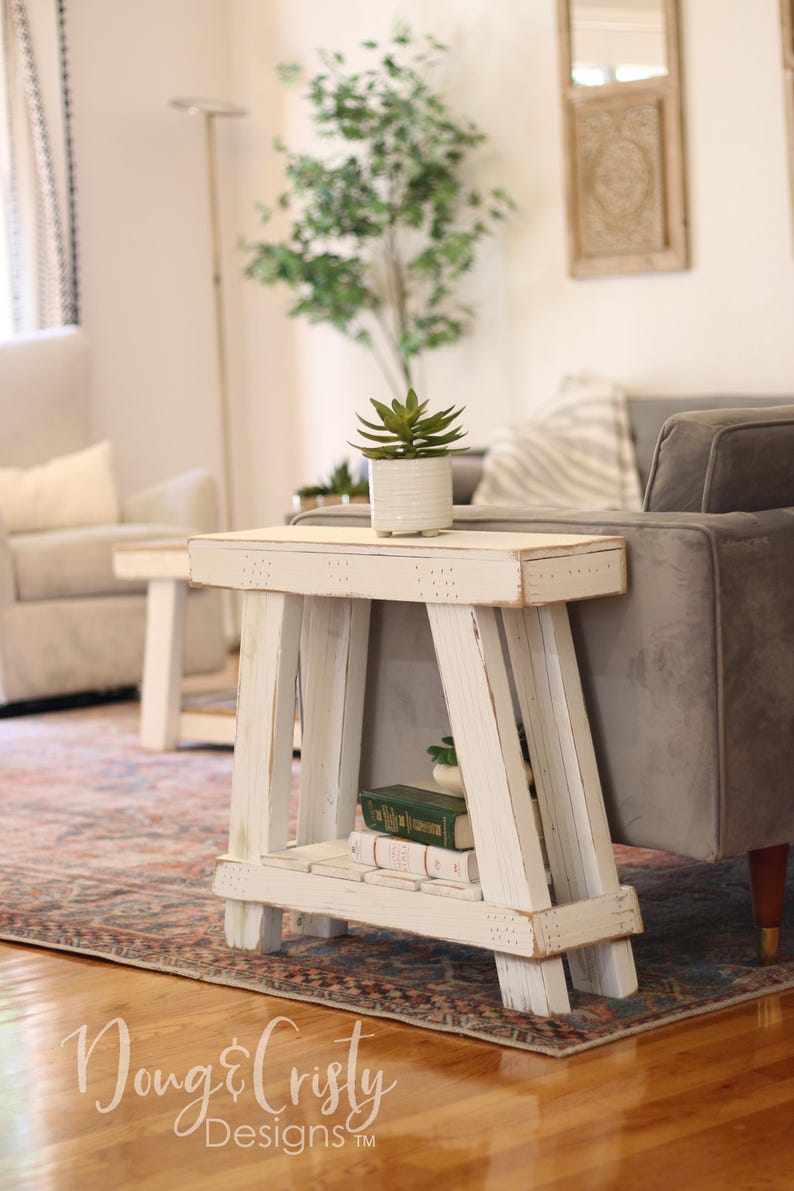 May include: White wooden side table with a distressed finish. The table has a shelf and a top surface. A small potted succulent plant sits on the top surface. The table is in a living room setting with a rug and a couch.