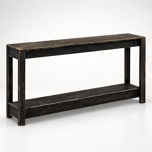 May include: A long, rectangular console table constructed from dark wood with a distressed black finish. The piece features a flat top surface supported by four straight legs and includes a single lower shelf positioned between the legs.