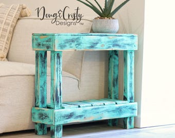 May include: A teal blue end table with a distressed finish and black accents. The table has a shelf and is made of wood.  Dong & Christy Designs™