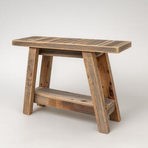 May include: A rustic wooden bench with a rectangular top and angled legs. The bench is made of reclaimed wood, showcasing natural grain and color variations. The bench is approximately 18 inches long, 12 inches wide, and 18 inches high.