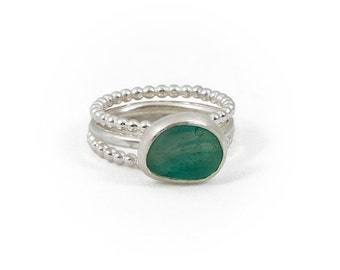 Puede incluir: Un anillo de plata con tres bandas, cada una con un borde de cuentas. La banda superior presenta una piedra de vidrio de mar verde.