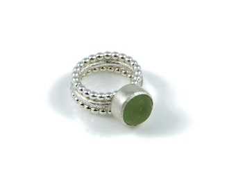 Puede incluir: Un anillo de plata con una piedra verde engastada en un bisel. La banda del anillo está hecha de tres filas de pequeñas cuentas de plata.