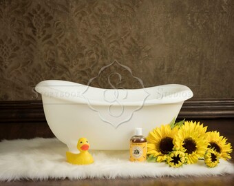 May include: A white bathtub with a yellow rubber ducky and a bottle of bath products on a white fluffy rug with sunflowers.