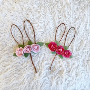 May include: Two brown wire bunny ears with pink and red fabric flowers attached. The flowers have green leaves.