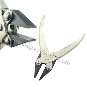 May include: A pair of silver-toned jewellery pliers with black rubberised jaws. The pliers have a textured handle and a spring-loaded mechanism.