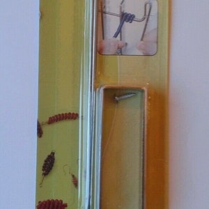 May include: A close-up of a packaging for a wire coiling tool. The packaging is yellow and green with the text "Artistic Wire" and "Coiling Gizmo Econo Winder". The tool is made of metal and is shown in the packaging. The packaging also includes instructions in English, French, and Spanish.