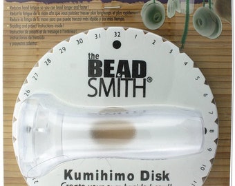 May include: White Kumihimo Disk with a clear plastic handle. The disk has numbers 1 through 32 around the edge. The text "Kumihimo Disk Create your own braided cord!" is printed on the disk. The text "Patent Pending USA, Canada, Europe" is printed on the packaging.
