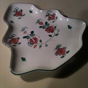 May include: White ceramic serving dish with a unique, irregular shape. The dish is decorated with red floral patterns and green leaves. A thin green line trims the edge of the dish.