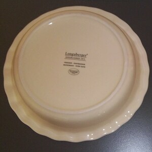 May include: Off-white pie plate with a scalloped edge. The bottom of the plate has the text "Longaberger ESTABLISHED 1973" and "FREEZER - DISHWASHER - MICROWAVE - OVEN SAFE".