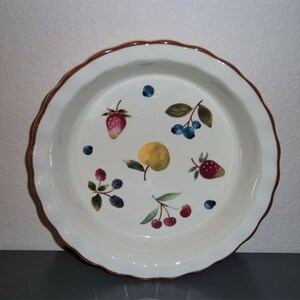 May include: White ceramic pie plate with a scalloped edge and a brown rim. The plate is decorated with colorful illustrations of various fruits, including strawberries, blueberries, cherries, and a lemon.